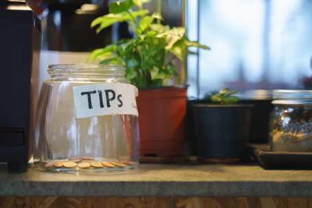 Glass tips jar in cafe with few Thai coins